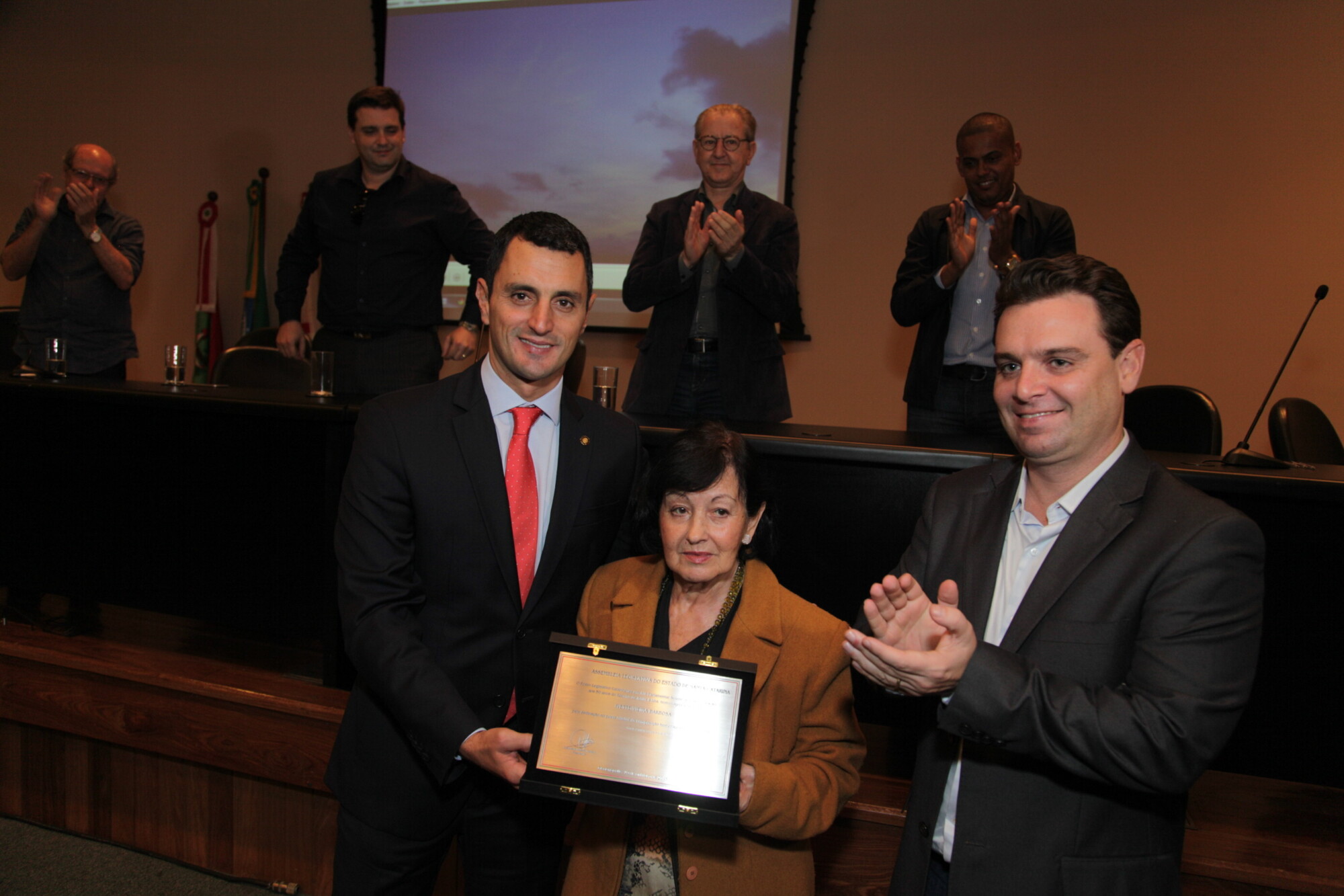 A viúva de Zininho, Ivette Barbosa, recebe a placa das mãos do deputado João Amim e do prefeito Cesar Souza Junior. FOTO: Solon Soares/Agência AL