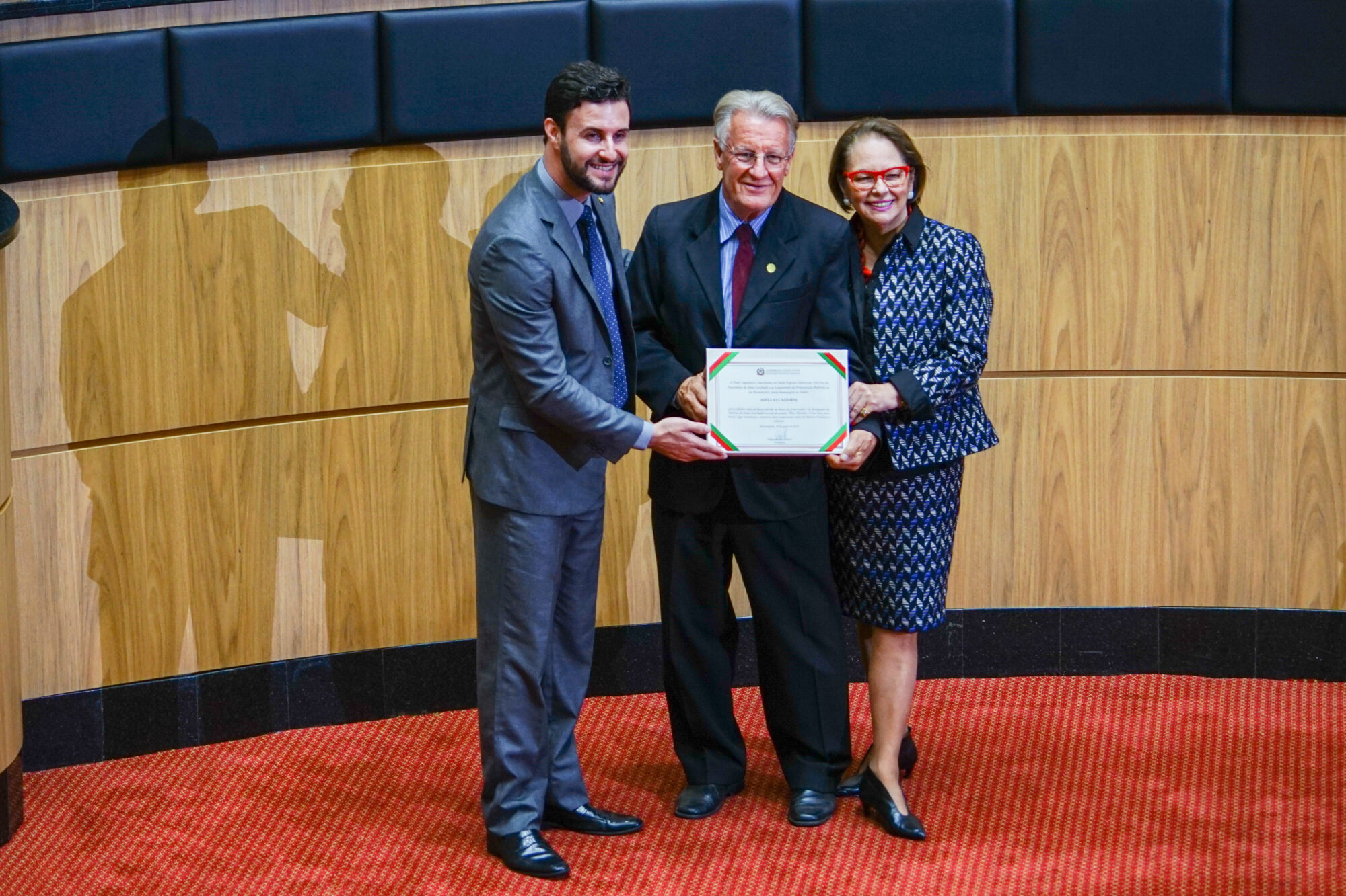 Historiador Adílcio Cadorin recebendo uma homenagem dos deputados Felipe Estevão e Ada de Luca.