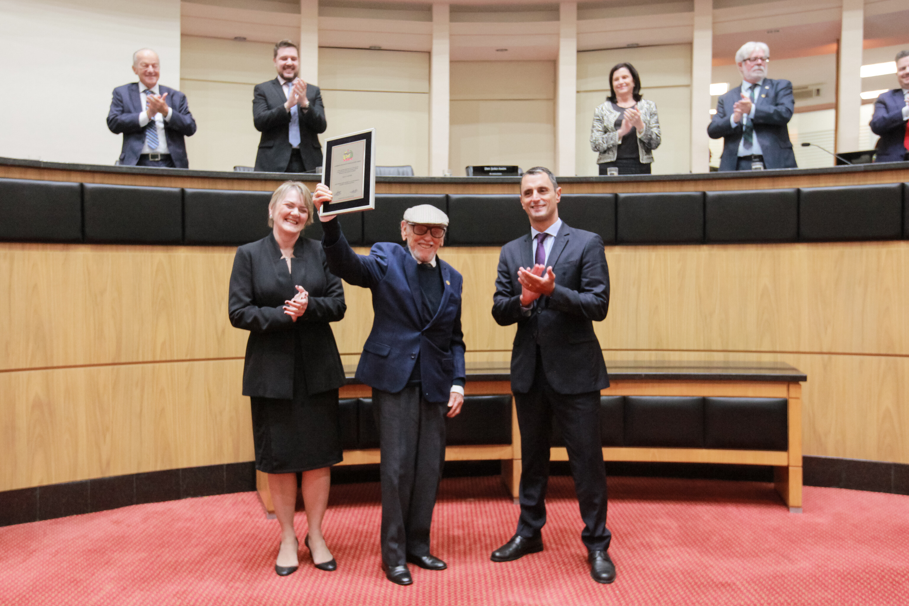 Os deputados Luciane Carminatti e João Amin entregaram uma placa comemorativa a Glauco Olinger, único representante vivo da primeira formação do CEE.